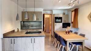 Una cocina moderna con una isla central, luces colgantes y un comedor con sillas y una mesa.