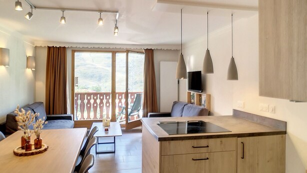 Cocina moderna con una isla central, comedor con mesa y sillas, y un balcón con vistas.