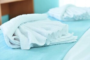 A neatly folded stack of white towels on a bed with a light blue bedspread. - Lovely Seaview Apartment in Chania (Apokoronas)