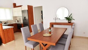 Un comedor moderno con una mesa de madera y sillas tapizadas grises, una cocina al fondo y un espejo redondo en la pared.
