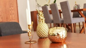 Una mesa de comedor con una vela blanca, una piña dorada y una manzana dorada.
