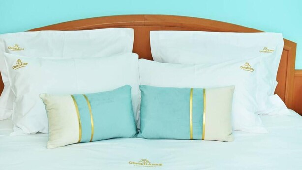 A bed with white and light blue pillows, a wooden headboard, and a plain wall in the background. - Christianna Luxury Apartment 2 (Apokoronas)