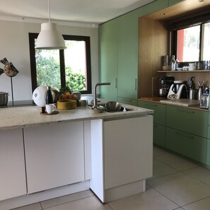 Een moderne keuken met een centraal eiland, groene kasten en een raam dat voor natuurlijk licht zorgt.