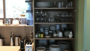 Et køkken med et vindue, hylder med service og en vanddispenser.