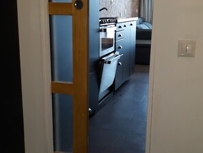 A kitchen with a built-in oven and a stove, a wooden door, and a tiled floor. - Renovated ski-in/ski-out studio with balcony, sleeps 5 (Les Arcs 2000)