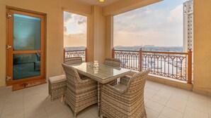 A balcony with a glass table and wicker chairs, offering a view of a cityscape and water. - Splendid View 2 Bedroom Apartment in the Palm Jumeirah (Dubai)