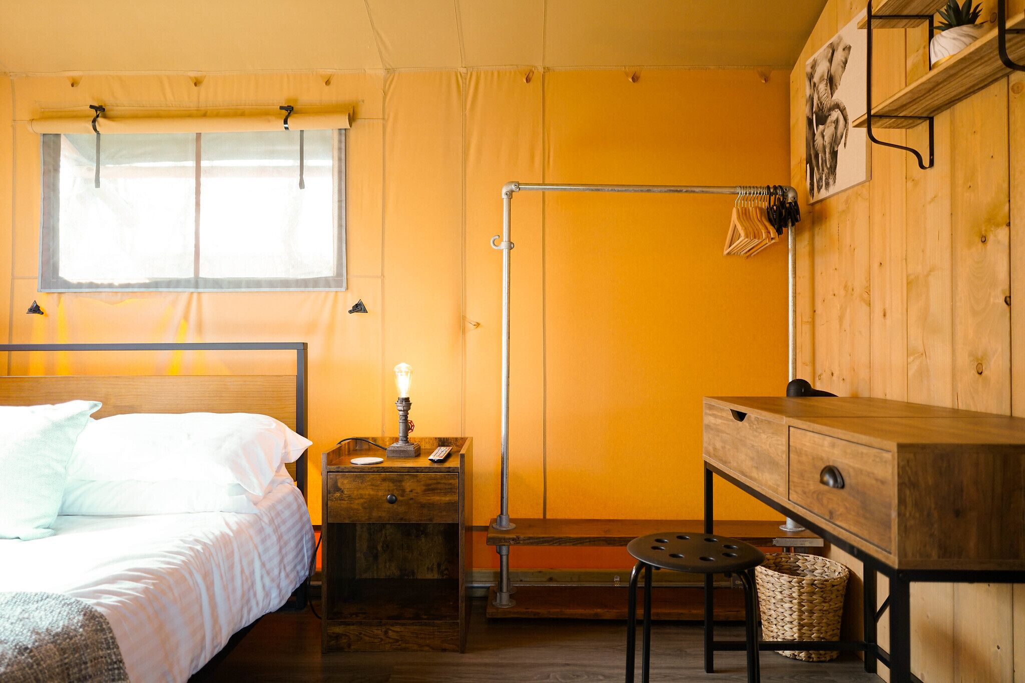 A room with a bed, a wooden desk, a lamp, and a hanging clothes rack.
