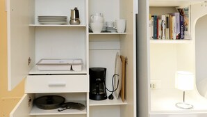 Eine Küche mit weißen Schränken, einer Kaffeemaschine, einem Wasserkocher und einem Bücherregal mit Büchern.