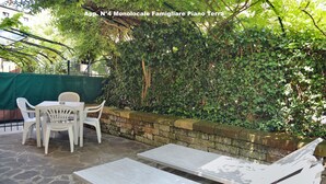 Eine Terrasse mit Steinboden, weißen Plastikstühlen und einem Tisch.