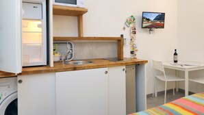 Eine kleine Küche mit einer Mikrowelle, Spüle und einer Holzarbeitsplatte. Neben der Arbeitsplatte steht ein kleiner Tisch mit einer Flasche und Papier.