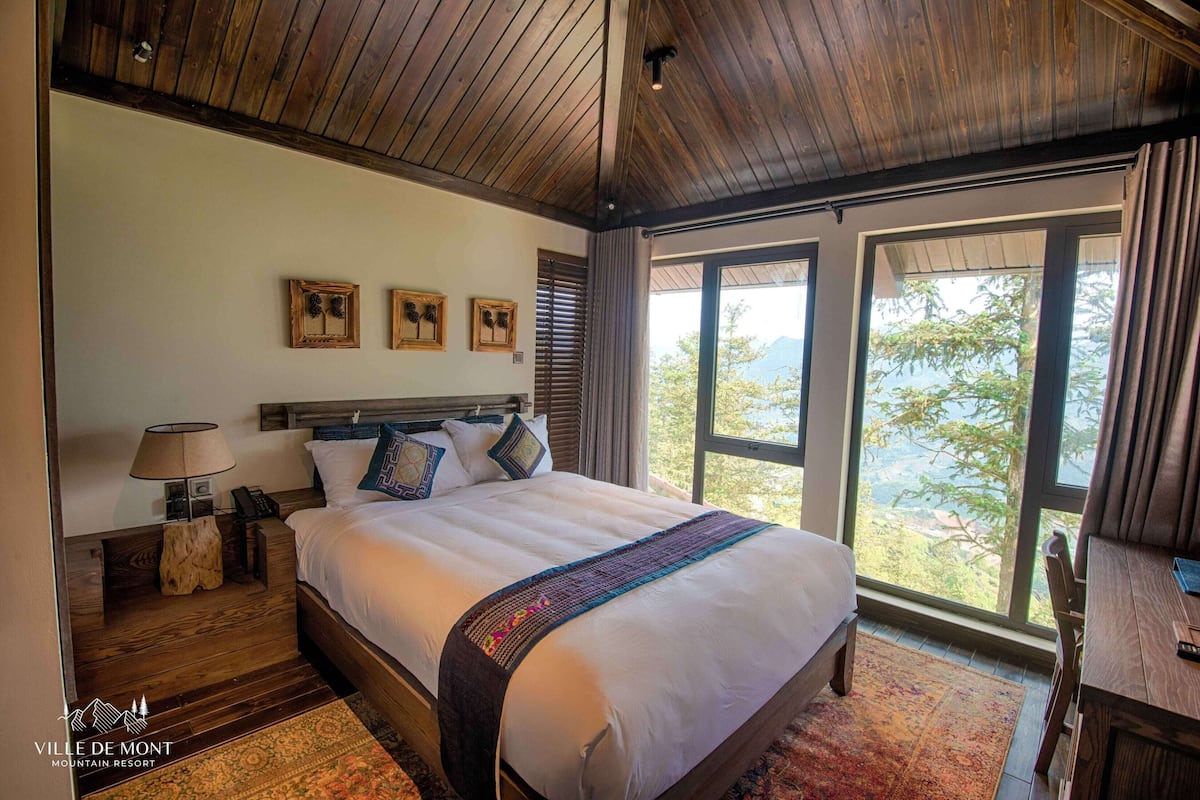 Un dormitorio con una cama grande, cabecero de madera y vistas al exterior a través de amplios ventanales.