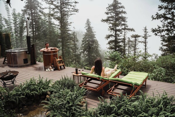 A wooden deck with lounge chairs, a hot tub, and a stone water feature surrounded by ferns.