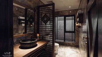 A bathroom with a stone sink, a toilet, and a window with blinds.