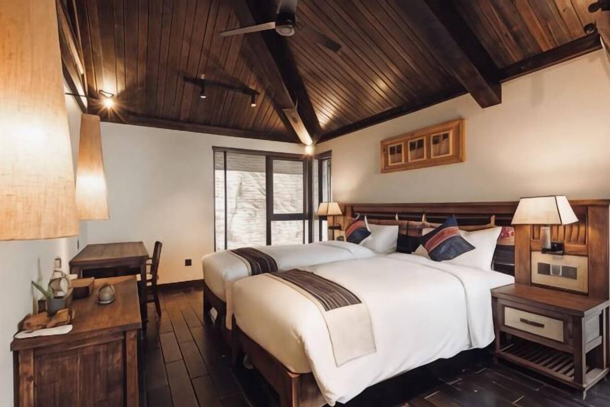 Una habitación con techo de madera, una cama con ropa blanca, una mesita de noche con lámpara y una ventana.