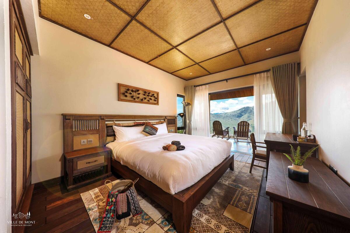 Un dormitorio con una cama grande, cabecera de madera, un escritorio y vistas a las montañas.