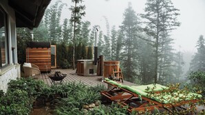 Een houten terras met loungezetels, een jacuzzi en een kleine waterval.