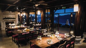 Een restaurant met meerdere eettafels en stoelen, een open haard en grote ramen met uitzicht op de bergen.