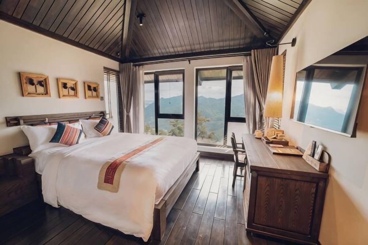 Un dormitorio con cama, muebles de madera, un escritorio y grandes ventanales con vista a la montaña.