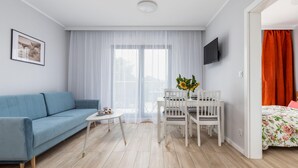 A modern living room with a blue sofa, a small white table, a white dining set, and a bed with floral bedding.