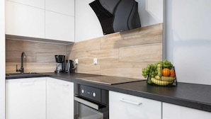 A modern kitchen with white cabinets, a black countertop, a coffee maker, and a fruit basket.