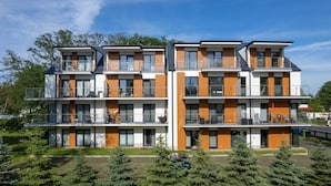 A modern multi-story residential building with balconies, large windows, and a mix of white and wooden paneling.