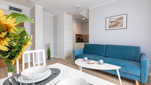 A modern living room with a blue sofa, a dining table set, and a kitchen in the background.