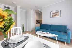 A modern living room with a blue sofa, a dining table set, and a kitchen in the background.