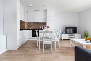 Eine moderne Küche mit weißen Schränken, einer Holz-Spritzschutzwand und einem Essbereich mit weißem Tisch und Stühlen.