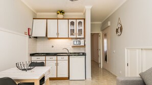 A compact kitchen with white cabinets, a microwave, and a dishwasher. There is a dining table with chairs and a decorative bowl. A gray sofa is visible in the foreground. - Saule Apartment, Swimming Pool, Terrace !new! (Lagos)