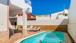 A swimming pool with a wooden deck and lounge chairs, surrounded by white buildings with balconies. - Saule Apartment, Swimming Pool, Terrace !new! (Lagos)