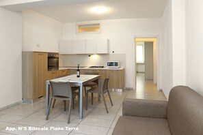 A compact kitchen with modern appliances, a dining area with a table and chairs, and a neutral-toned living space with a sofa.