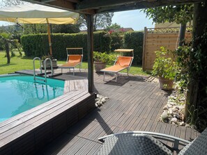 A wooden deck with a pool, two lounge chairs, and a pergola with a canopy.