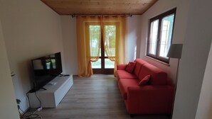 A living room with a television, a red sofa, and a window with curtains. - House I Limori with garden and parking (Gello)