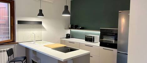 Una cocina moderna con una isla central, iluminación colgante, horno empotrado y refrigerador.