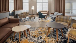 Un moderno hall de hotel con un sofá de cuero marrón, varios sillones, una mesa de centro redonda y un gran ventanal que aporta luz natural.
