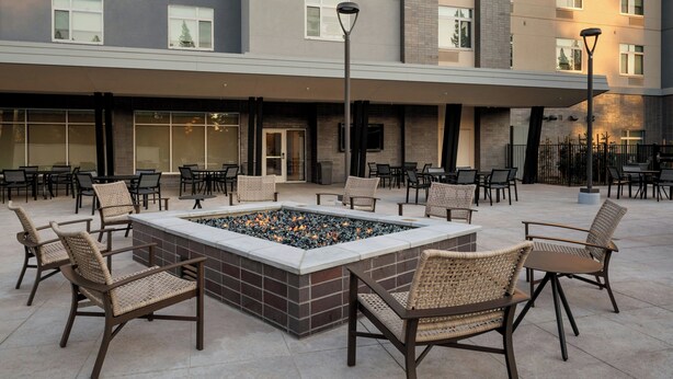 Un patio al aire libre con una chimenea, asientos y un edificio al fondo.
