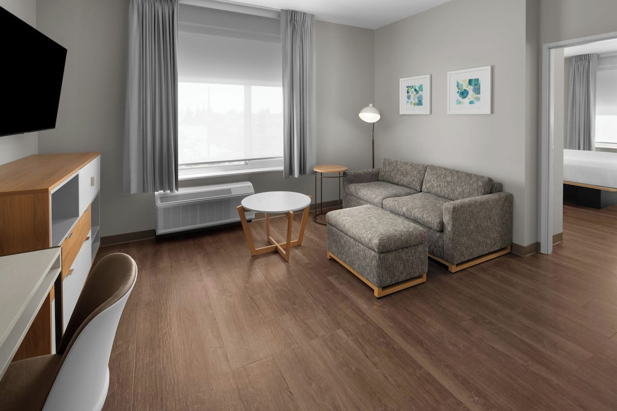 Een moderne hotelkamer met een bank, een klein rond tafeltje, een televisie en een raam met gordijnen.