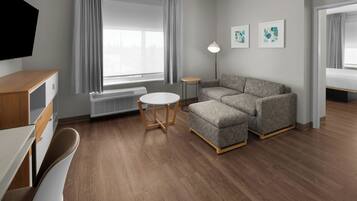 Une chambre d’hôtel moderne avec un canapé, une petite table ronde, un téléviseur et une fenêtre avec des rideaux.