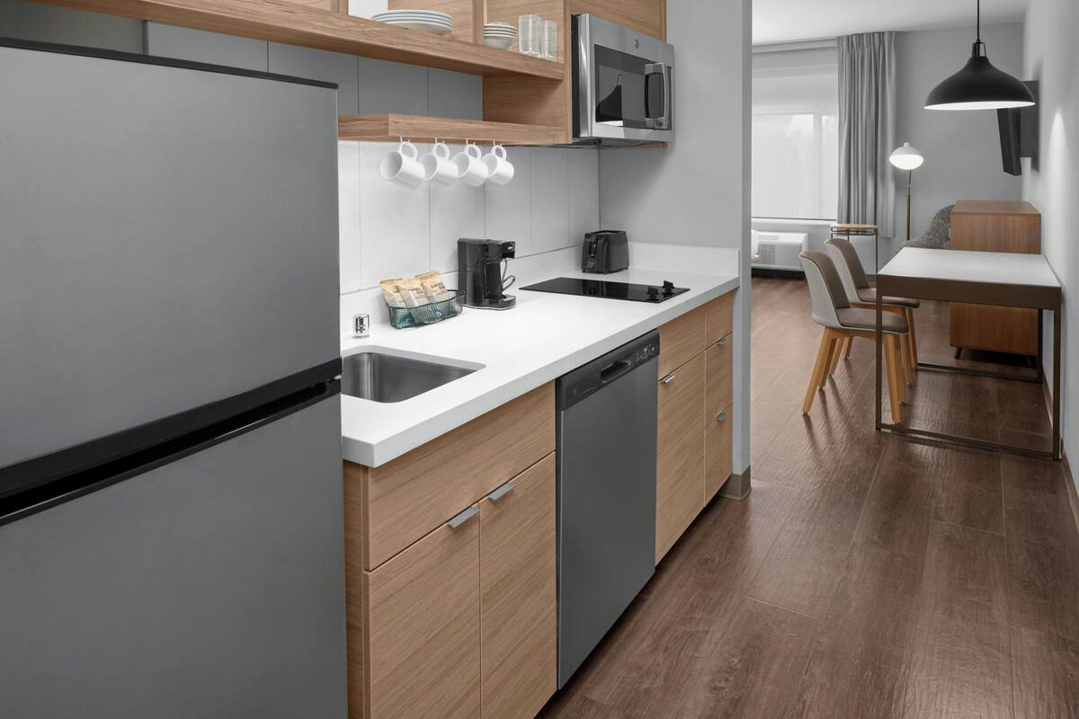 Een moderne keuken met een vaatwasser, een koffiezetapparaat en een magnetron. Er is een eethoek met een tafel en stoelen.