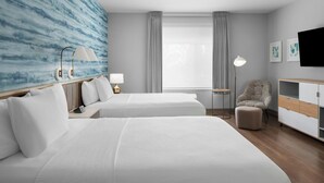 Habitación de hotel con dos camas, un escritorio, una silla, un televisor y un ventanal con cortinas.