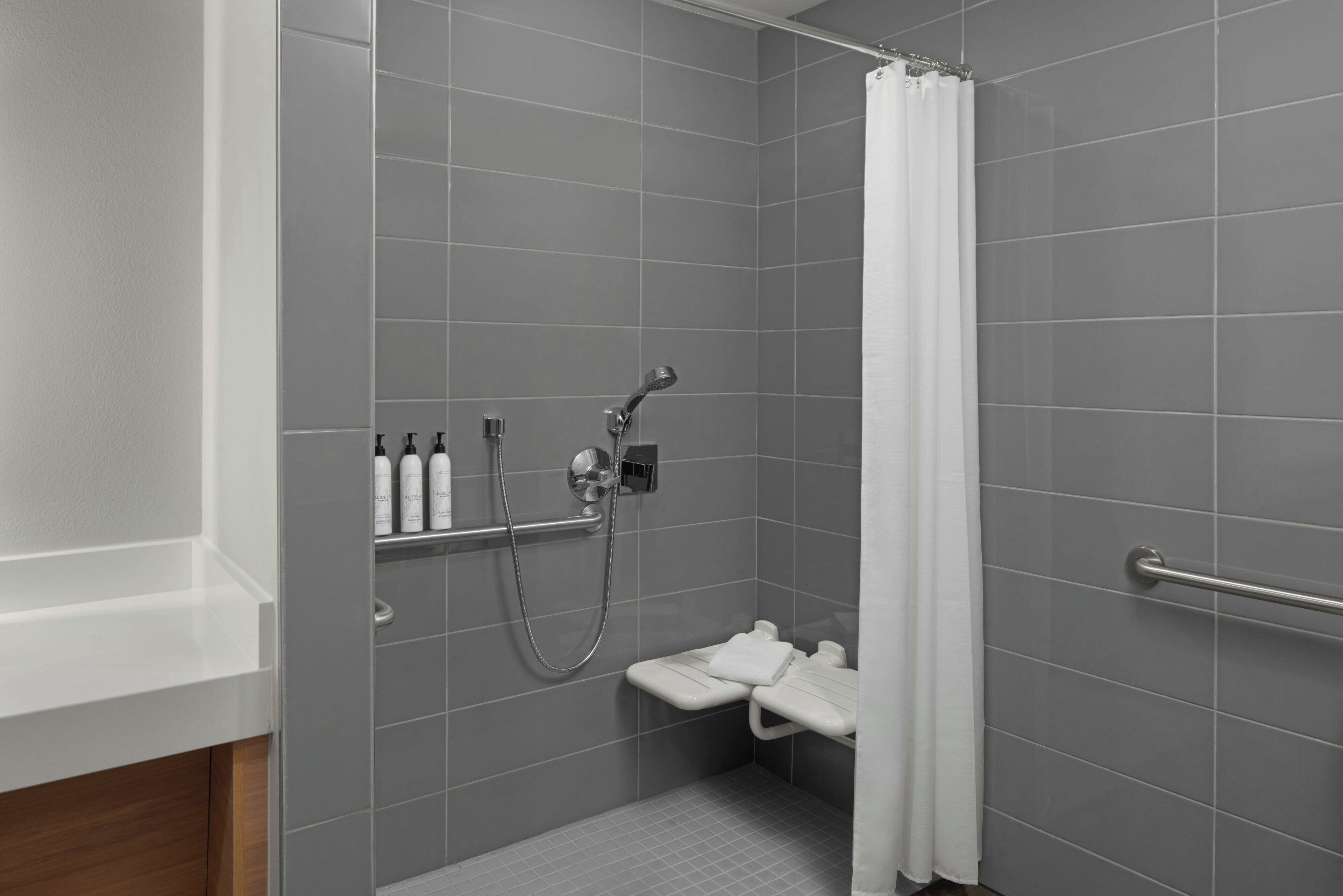 Un área de ducha moderna con azulejos grises, una cortina de ducha blanca y una barra de apoyo.