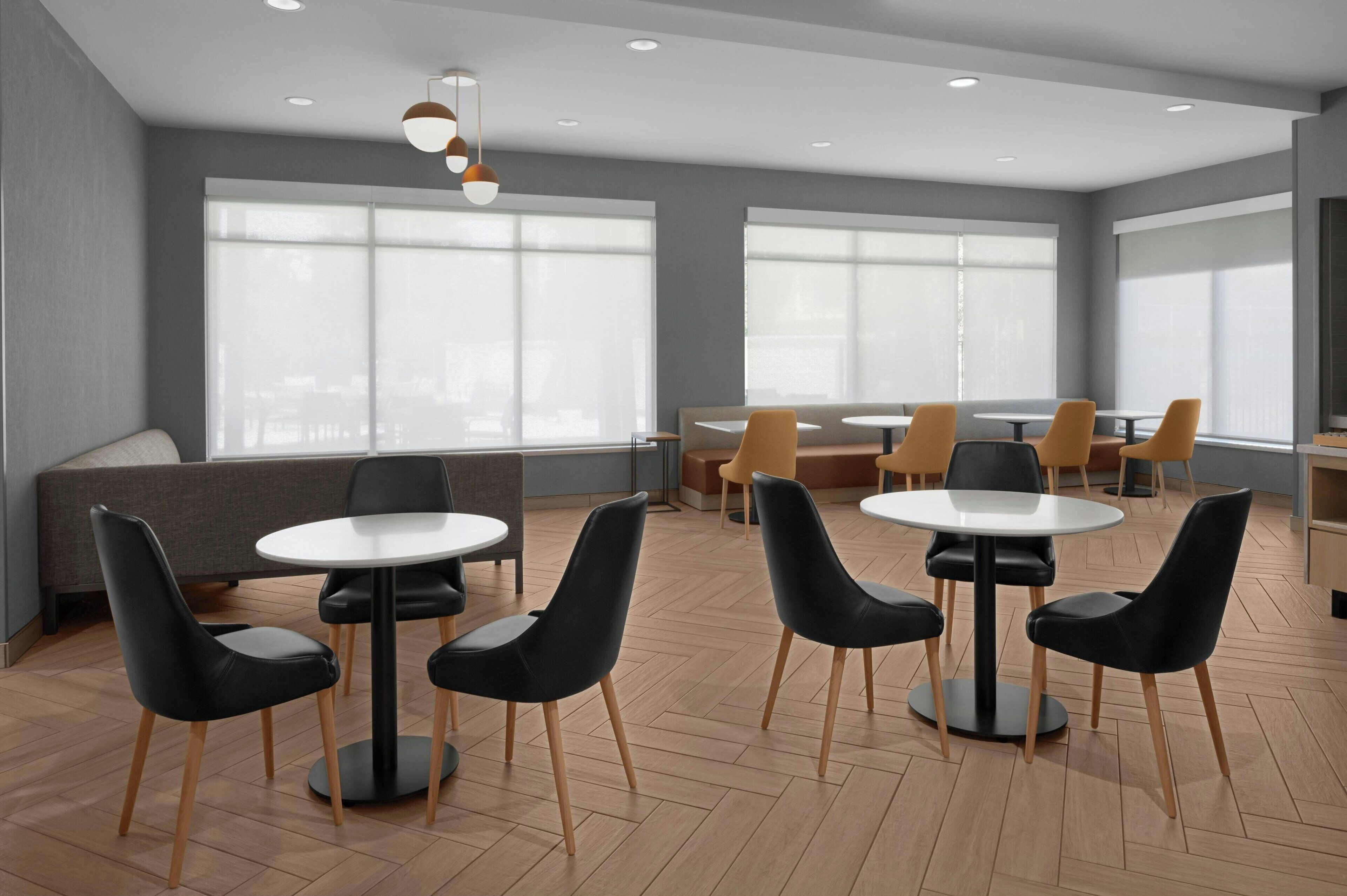 A modern dining area with round tables and black chairs, large windows, and a grey wall.