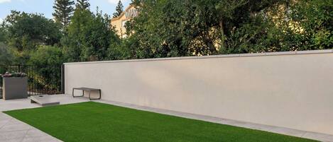 Un patio exterior moderno con césped artificial, un banco minimalista y un muro bajo.