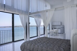 Un dormitorio con una cama grande, un balcón con vista al mar y una pequeña kitchenette.