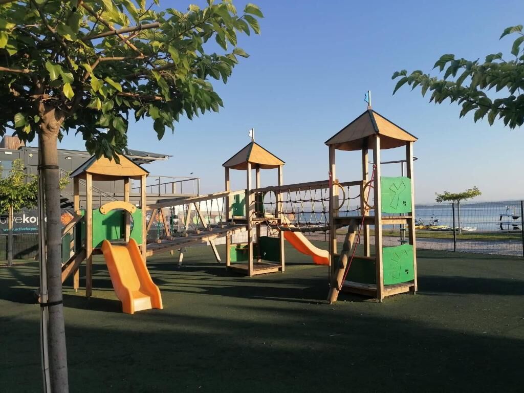 Un parque infantil con varias estructuras de juego, incluyendo toboganes y zonas de escalada, rodeado por una valla.