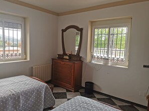 A bedroom with two beds, a dresser, a mirror, and two windows with balconies.
