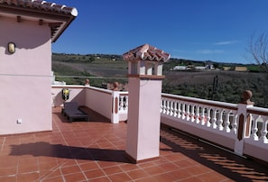 A terrace with a tiled floor, white balustrade, and a view of a rural landscape.
