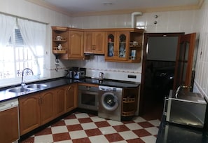 A kitchen with wooden cabinets, a washing machine, a refrigerator, and a sink.