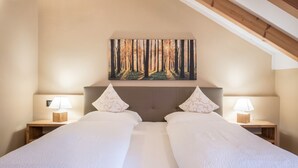 A double bed with a headboard, two bedside tables with lamps, and a forest painting above the bed.