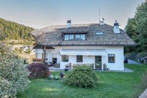 A two-story house with a sloped roof, a covered porch, and a small garden with various plants and a lawn. - 'Lotschenhof Apartment Tulpe' with Mountain View, Garden & Wi-Fi (Trodena)